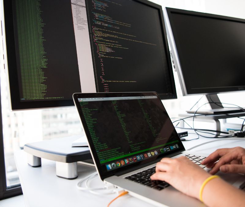 An IT technician typing on a computer behind three screen